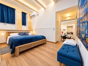 A bedroom with a bed, a bench, a dining area, and a kitchen. - The advantages of a detached house with services and quality of a boutique hotel (Il-Belt Valletta)