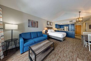 A hotel room with a bed, a blue sofa, a small table, a desk, and a kitchenette. - 2BR Winter Wonderland (Park City)