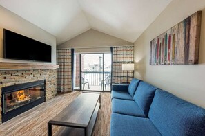 Ein Wohnzimmer mit Kamin, einer Couch, einem an der Wand befestigten Fernseher und einem Balkon mit Vorhängen.