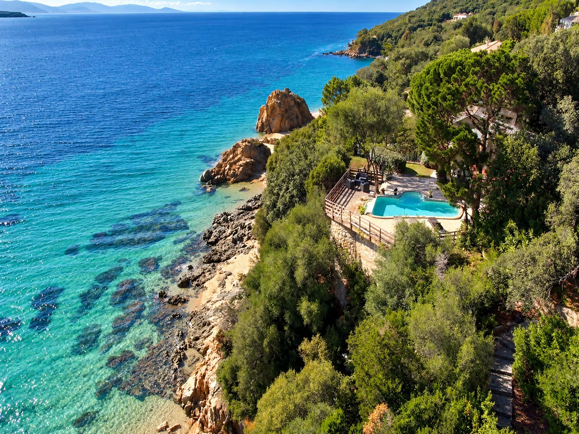 A coastal property with a swimming pool, rocky shoreline, and lush greenery.