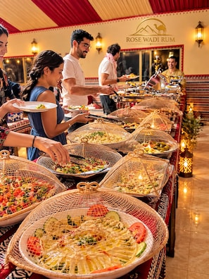 Buffet amb diversos plats dins cistells de veta, un rètol que diu 'ROSE WADI RUM' i una atmosfera interior acollidora.