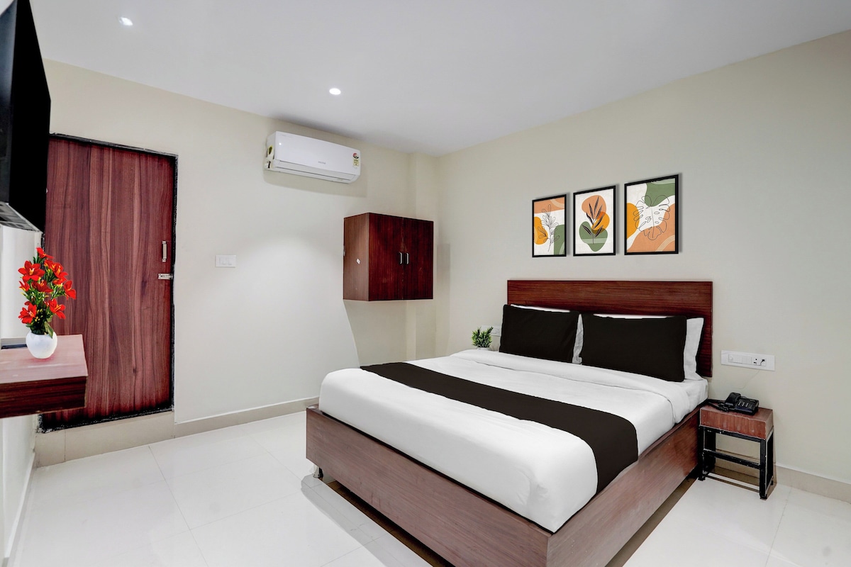 A hotel room with a bed, a nightstand, a telephone, an air conditioner, a cabinet, and a wall-mounted artwork.