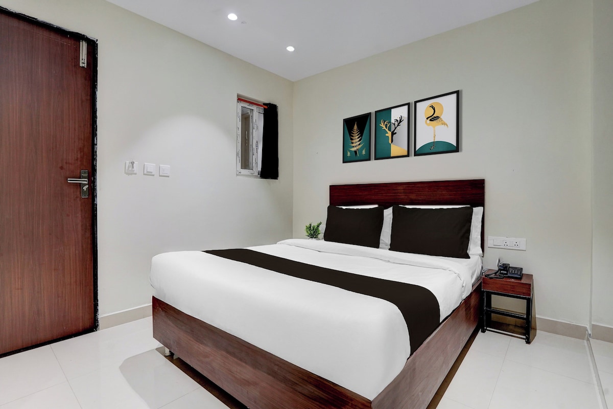 A hotel room with a large bed, a wooden headboard, a bedside table with a phone, and artwork on the wall.