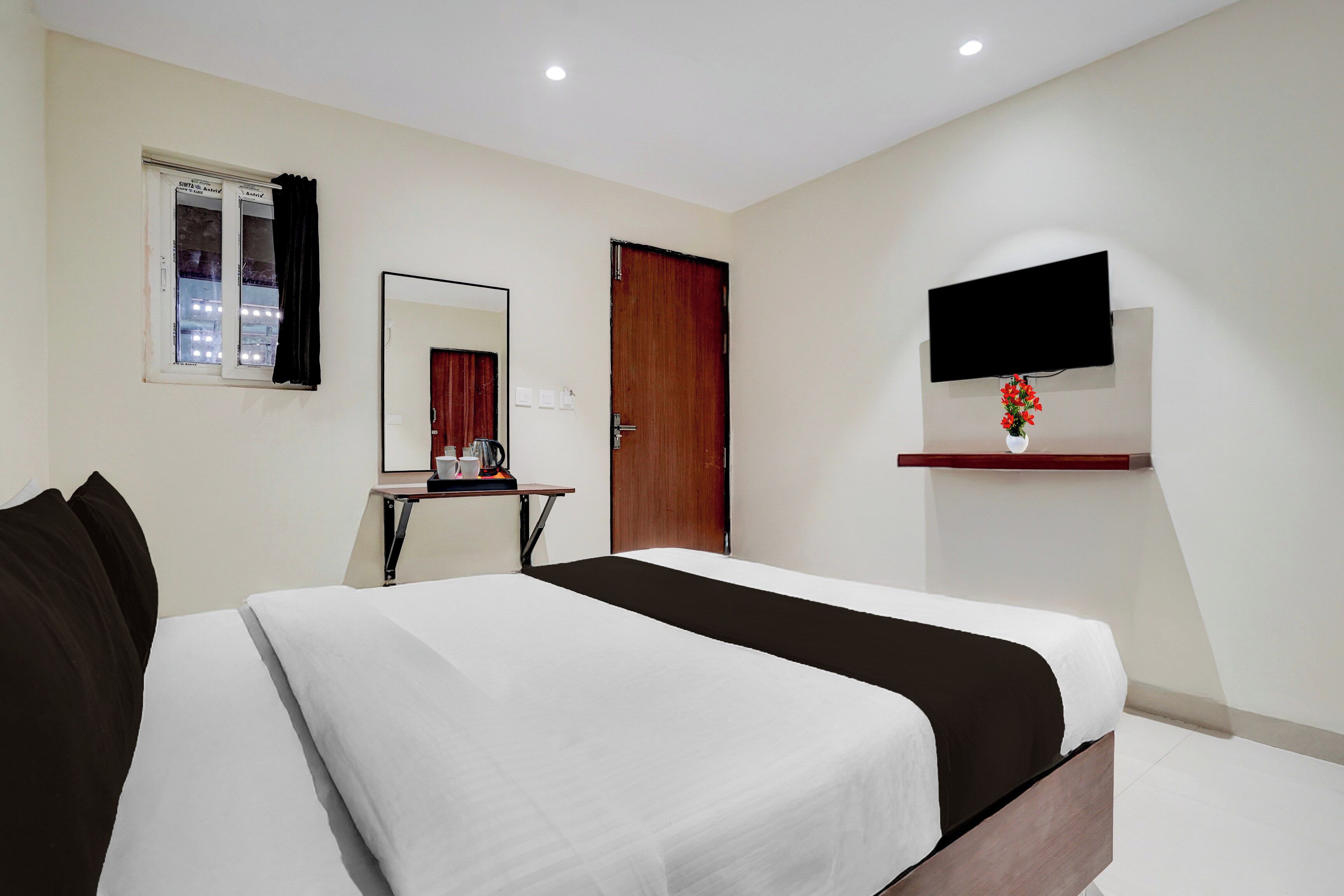 A hotel room with a bed, a desk, a mirror, a door, and a TV mounted on the wall.