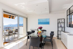 A modern dining area with a glass table, black chairs, and a view of the sea through large windows. - 3-Bedroom Apartment with Ocean View Terrace, Parking, 5 min from the Croisette A3B138 (Cannes)