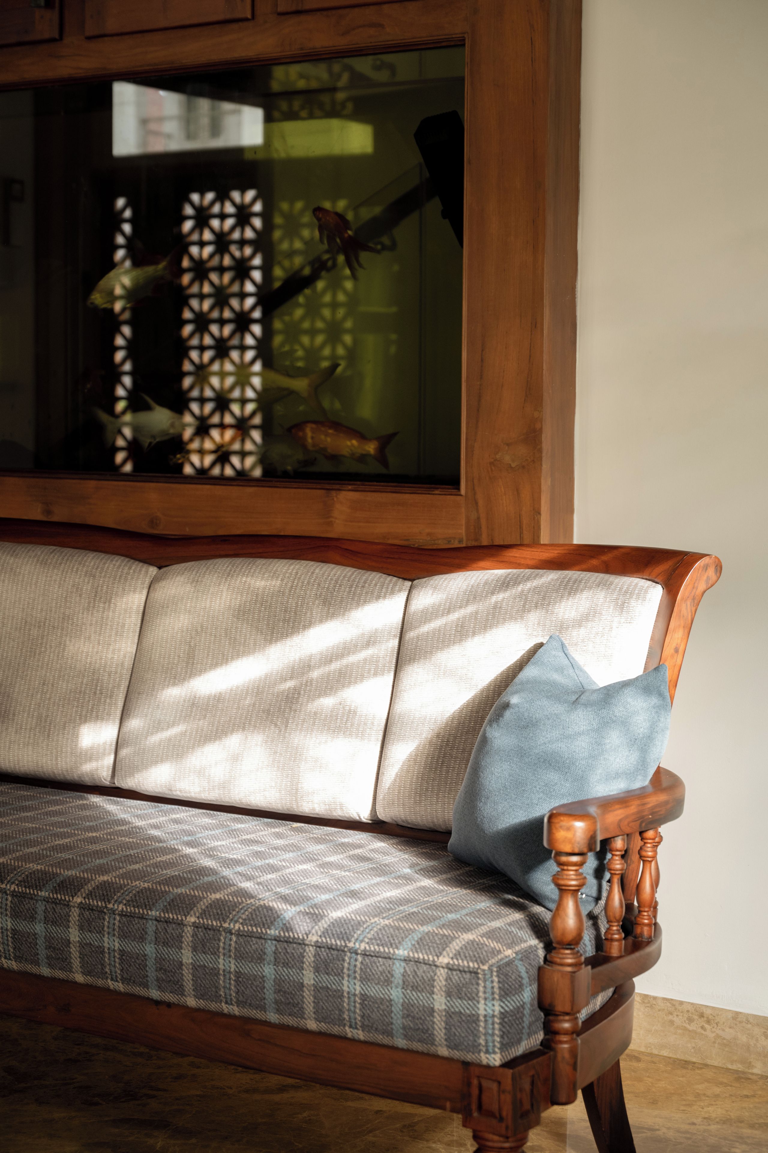A wooden bench with a plaid cushion and a single blue pillow.