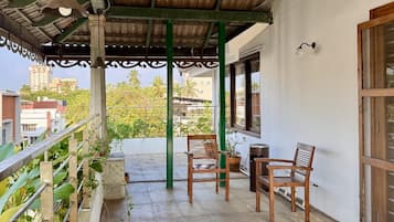 A covered balcony with a view of the city, featuring a table and chairs, and a railing with plants.
