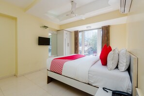 A hotel room with a bed, a TV, a ceiling fan, and a window with curtains.