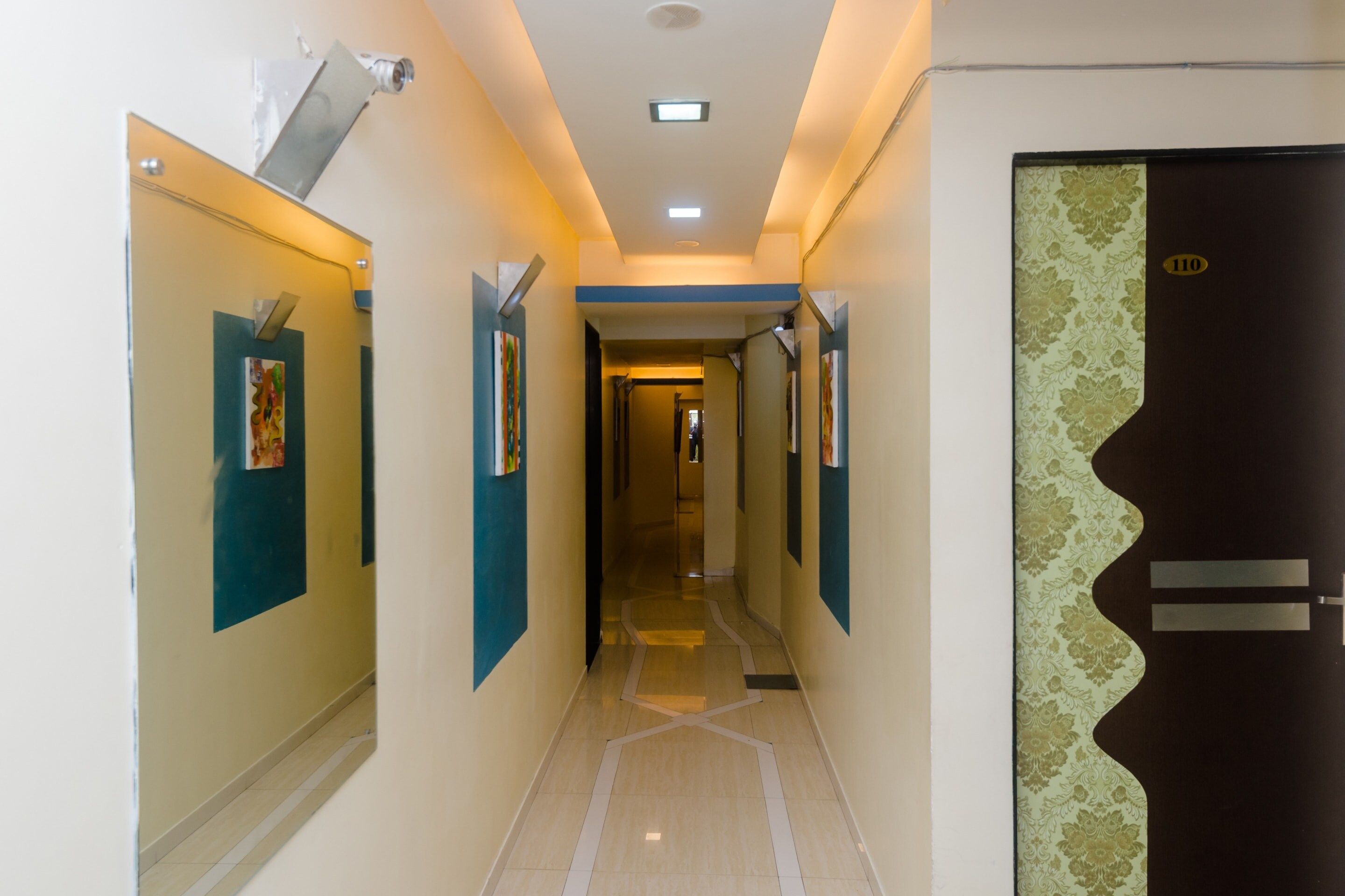 A hallway with a tiled floor, walls with artwork, and a door with a number plate.