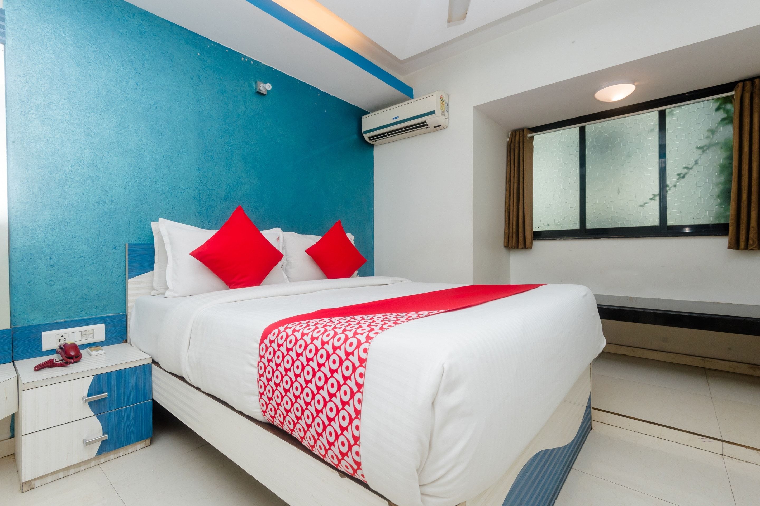 Een hotelkamer met een bed, nachtkastje, airconditioning en een raam met uitzicht.