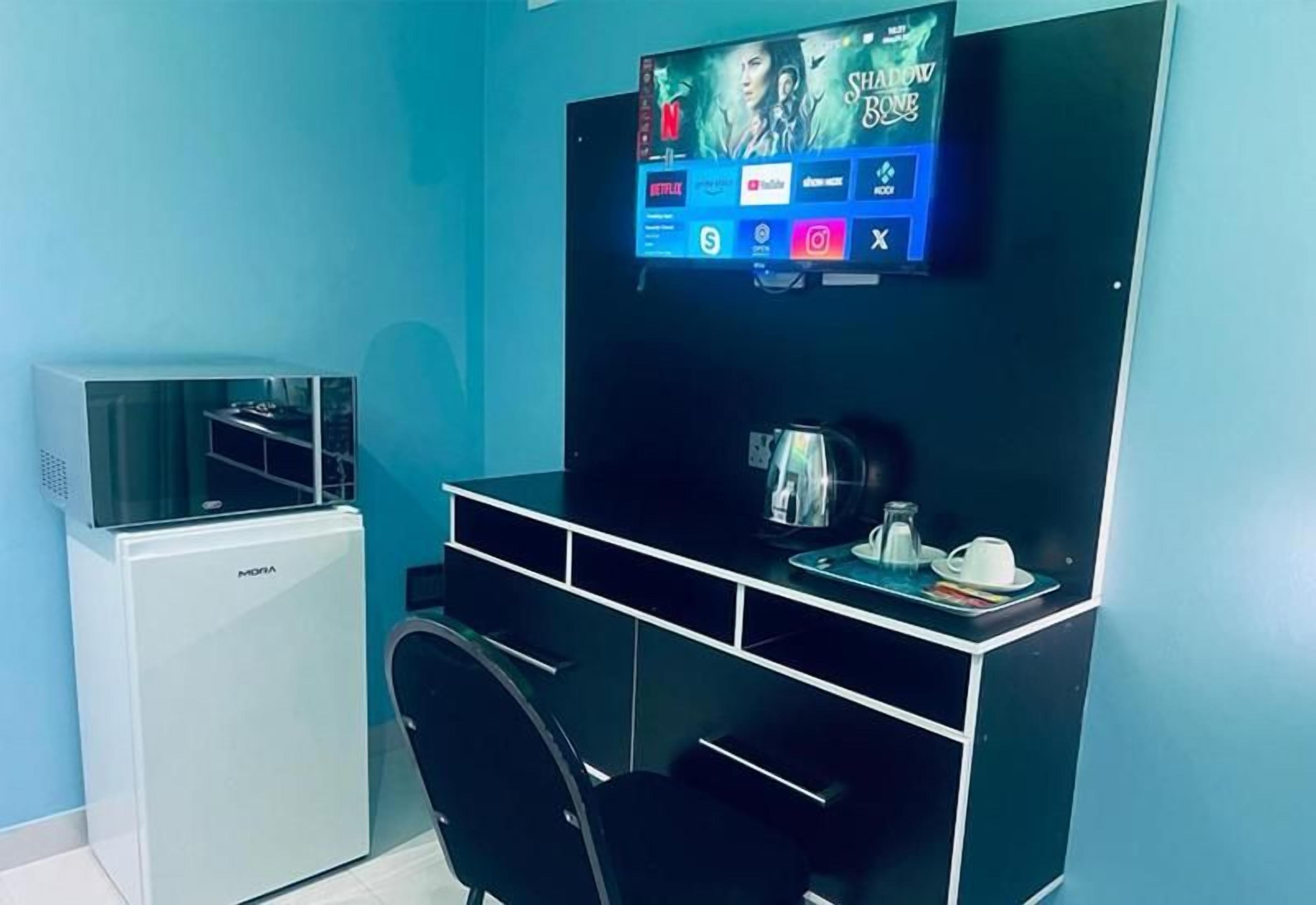 Una stanza con una scrivania nera, un condizionatore d'aria bianco, una televisione a muro e una macchina da caffè sulla scrivania.