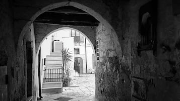 A narrow stone pathway leading through an arched doorway, flanked by buildings with visible windows and doors.