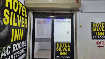 A hotel entrance with signs indicating 'Hotel Silver Inn AC Rooms' and a directional arrow pointing to the right.
