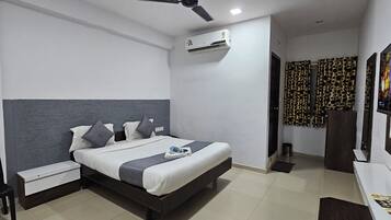 A hotel room with a bed, a desk, a chair, an air conditioner, and a television.