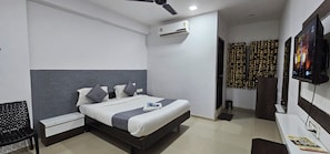 Una habitación de hotel con una cama, un escritorio, una silla, aire acondicionado y un televisor.