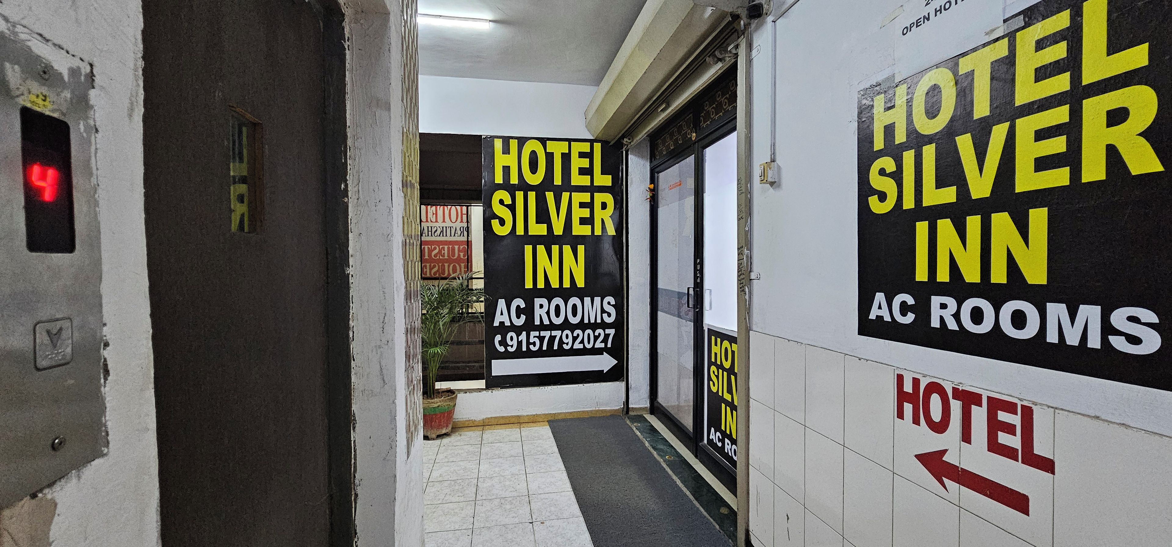 A hallway with signs for Hotel Silver Inn and AC rooms, a fire alarm, and a potted plant.