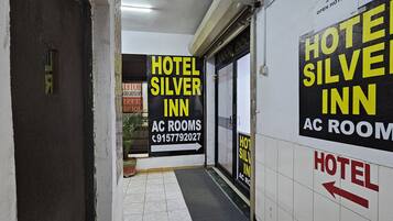 A hallway with signs for Hotel Silver Inn and AC rooms, a fire alarm, and a potted plant.