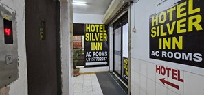 A hallway with signs for Hotel Silver Inn and AC rooms, a fire alarm, and a potted plant. - Hotel Silver Inn (Ahmedabad)