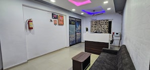 A reception area with a sofa, a small table, a fire extinguisher, a clock, and a ceiling fan. - Hotel Silver Inn (Ahmedabad)