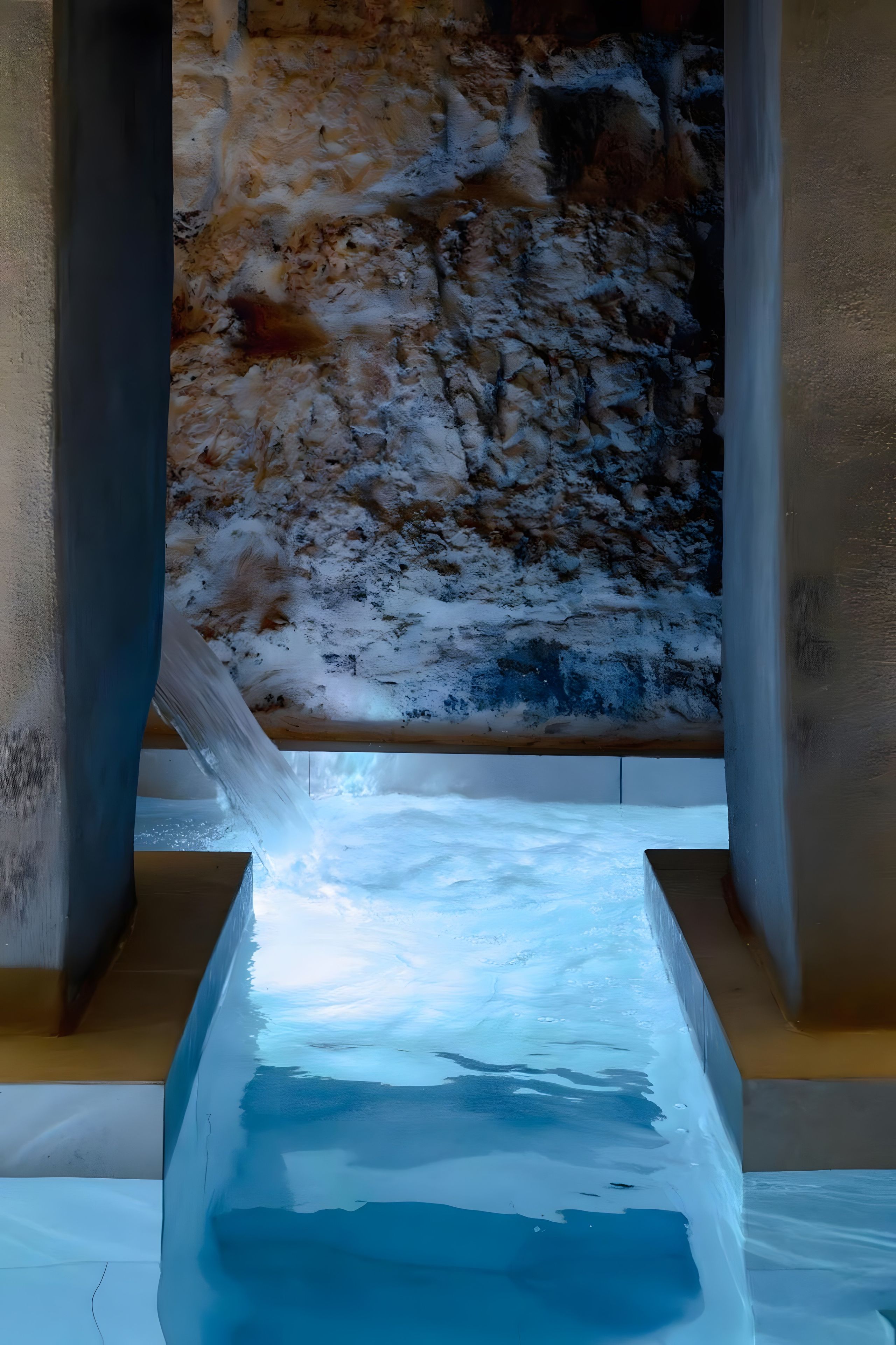 Una vasca di ghiaccio rettangolare con superficie d'acqua di colore blu intenso, circondata da un muro in pietra dalla texture grezza.