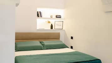Una camera da letto con un letto, un comodino, uno scaffale con libri e un vaso, e una porta ad arco.