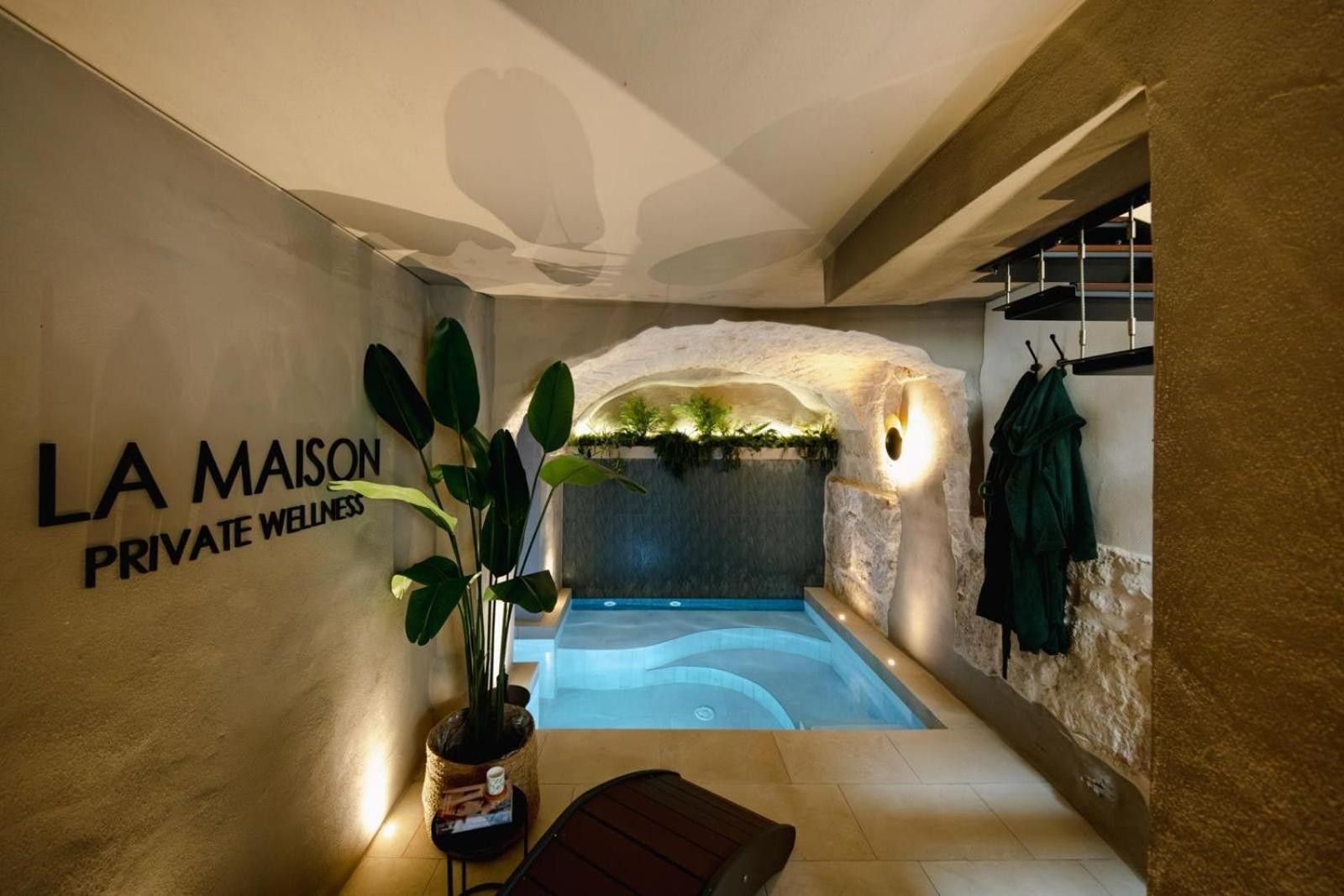 A private wellness area with a spa tub, a potted plant, and a wall-mounted sign reading 'LA MAISON PRIVATE WELLNESS.'