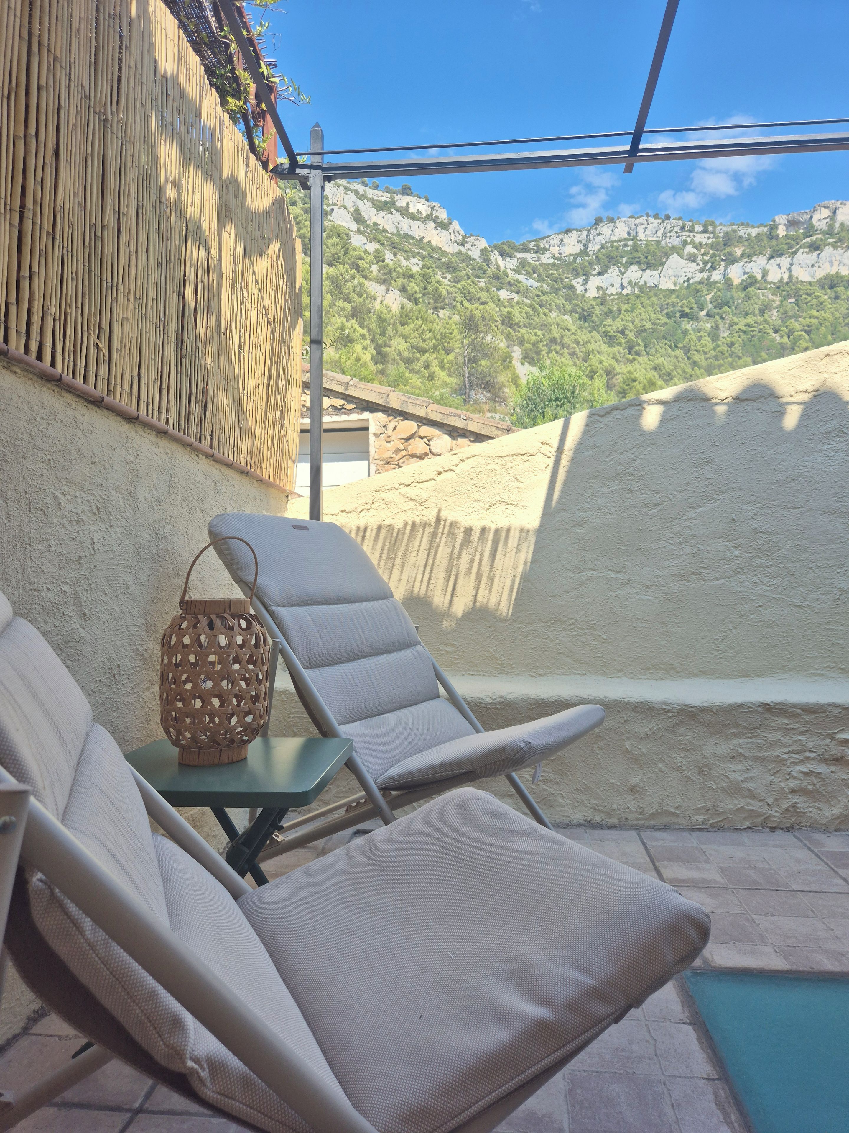 Un espacio al aire libre con luz solar, con dos sillones de descanso y una pequeña mesa, con vistas a un paisaje montañoso.
