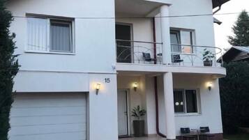 Una casa de dos pisos con garaje, balcón y entrada pavimentada.