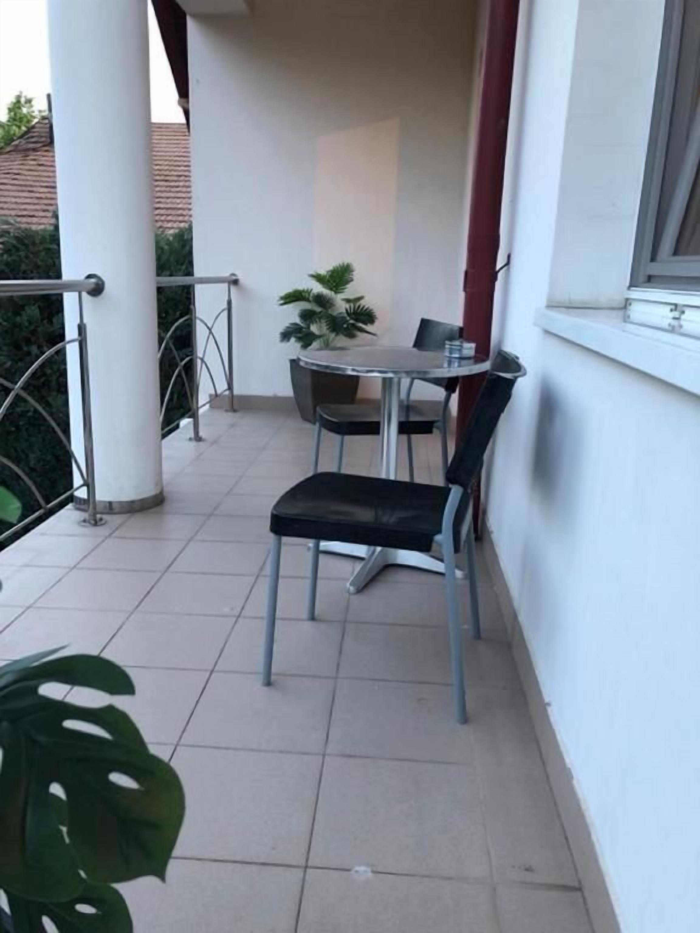 Un balcon avec une table et deux chaises, une plante en pot et une fenêtre.