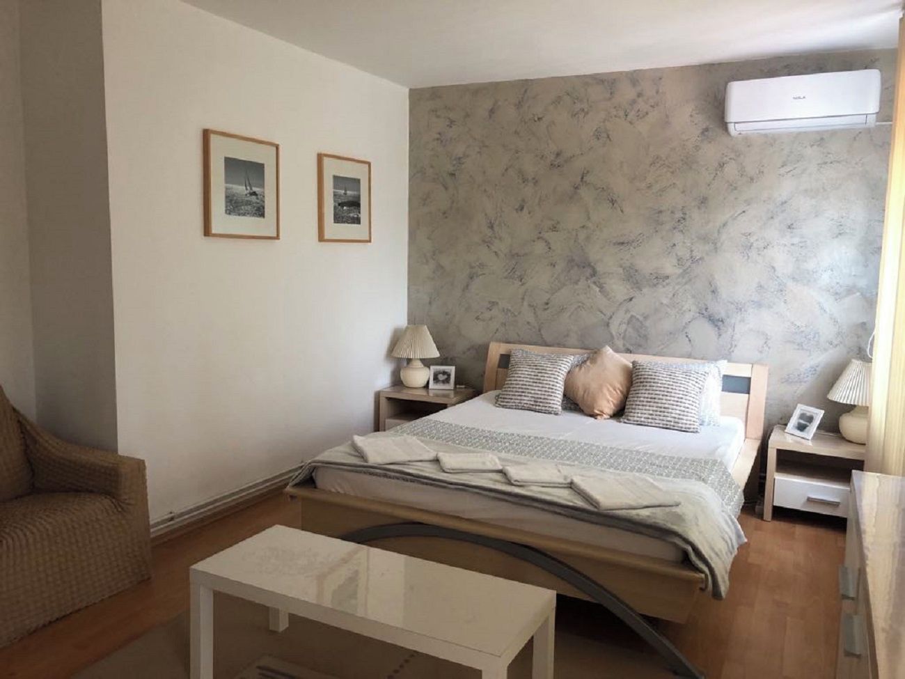 A bedroom with a bed, bedside tables, a chair, and a wall-mounted air conditioner.