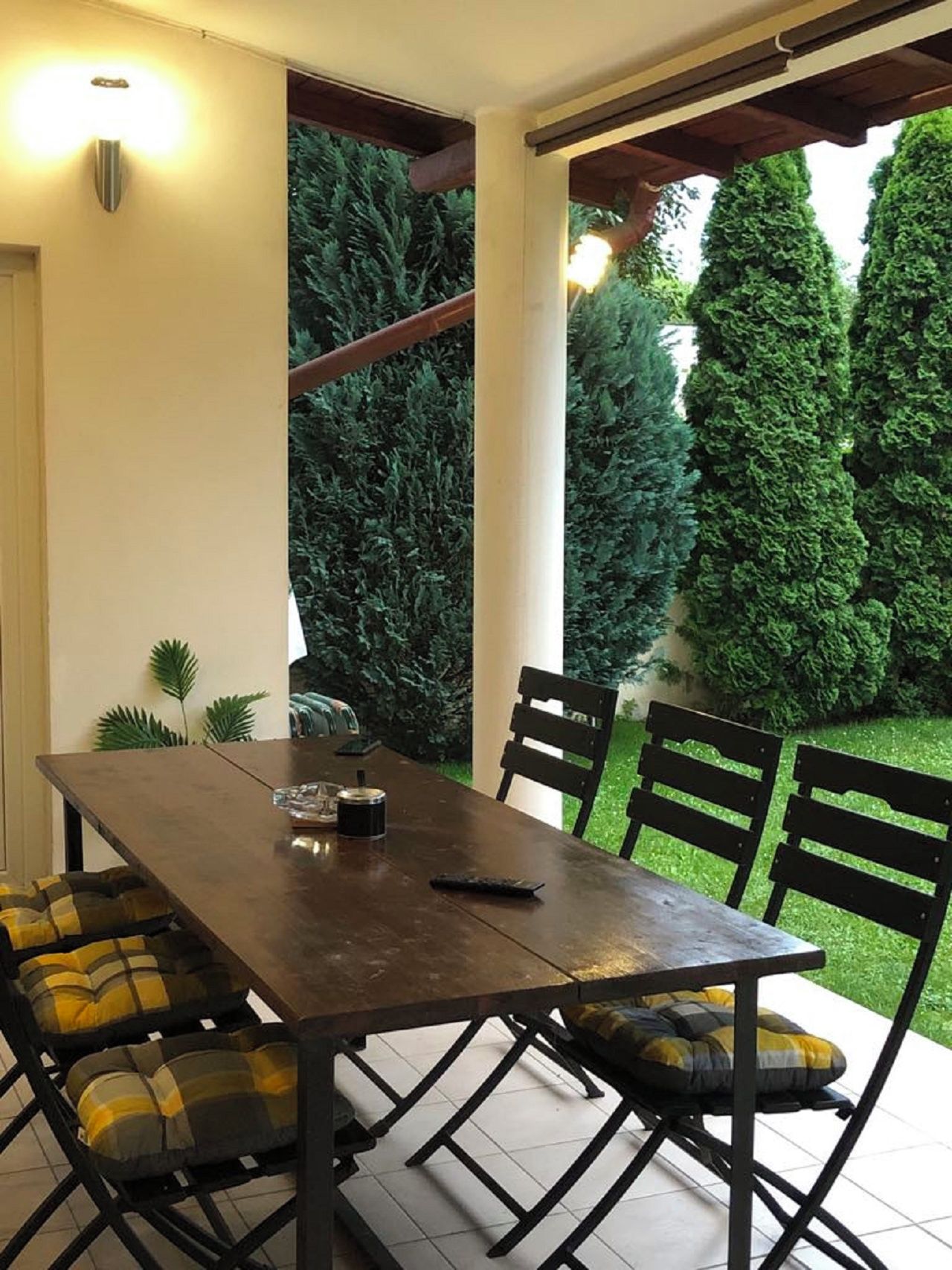 An outdoor dining area with a wooden table and chairs, surrounded by greenery.