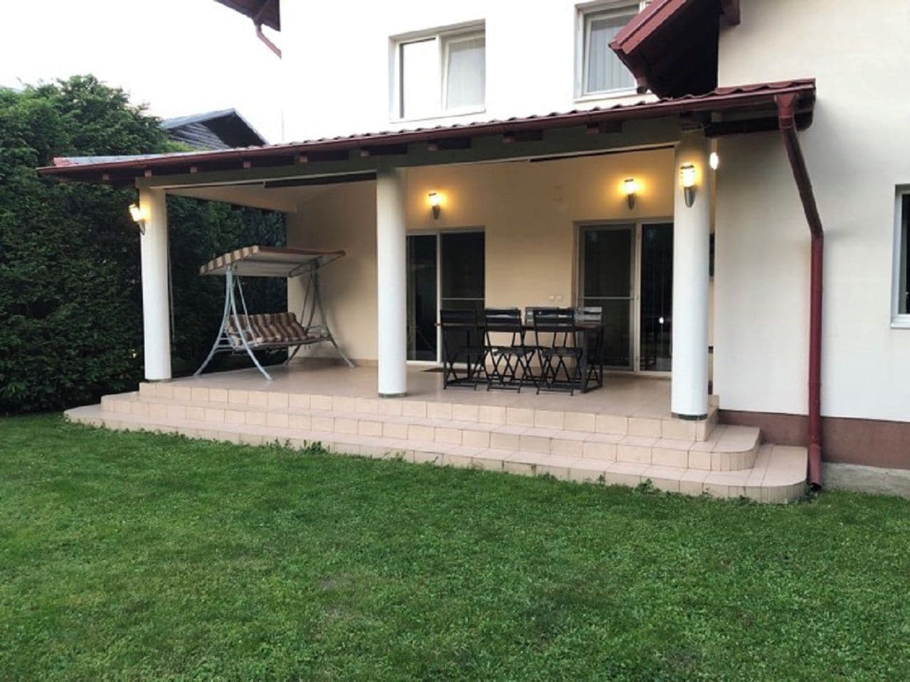 A covered patio with a table and chairs, a hanging chair, and a small outdoor area with steps leading to a door.