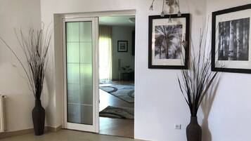 Un espacio interior con un divisor de vidrio corredizo que da a otra habitación, dos jarrones en el suelo y cuadros en la pared.