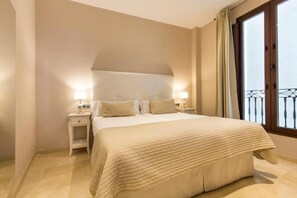 Habitación de hotel con una cama grande, dos mesitas de noche con lámparas, una ventana con vistas y un balcón.