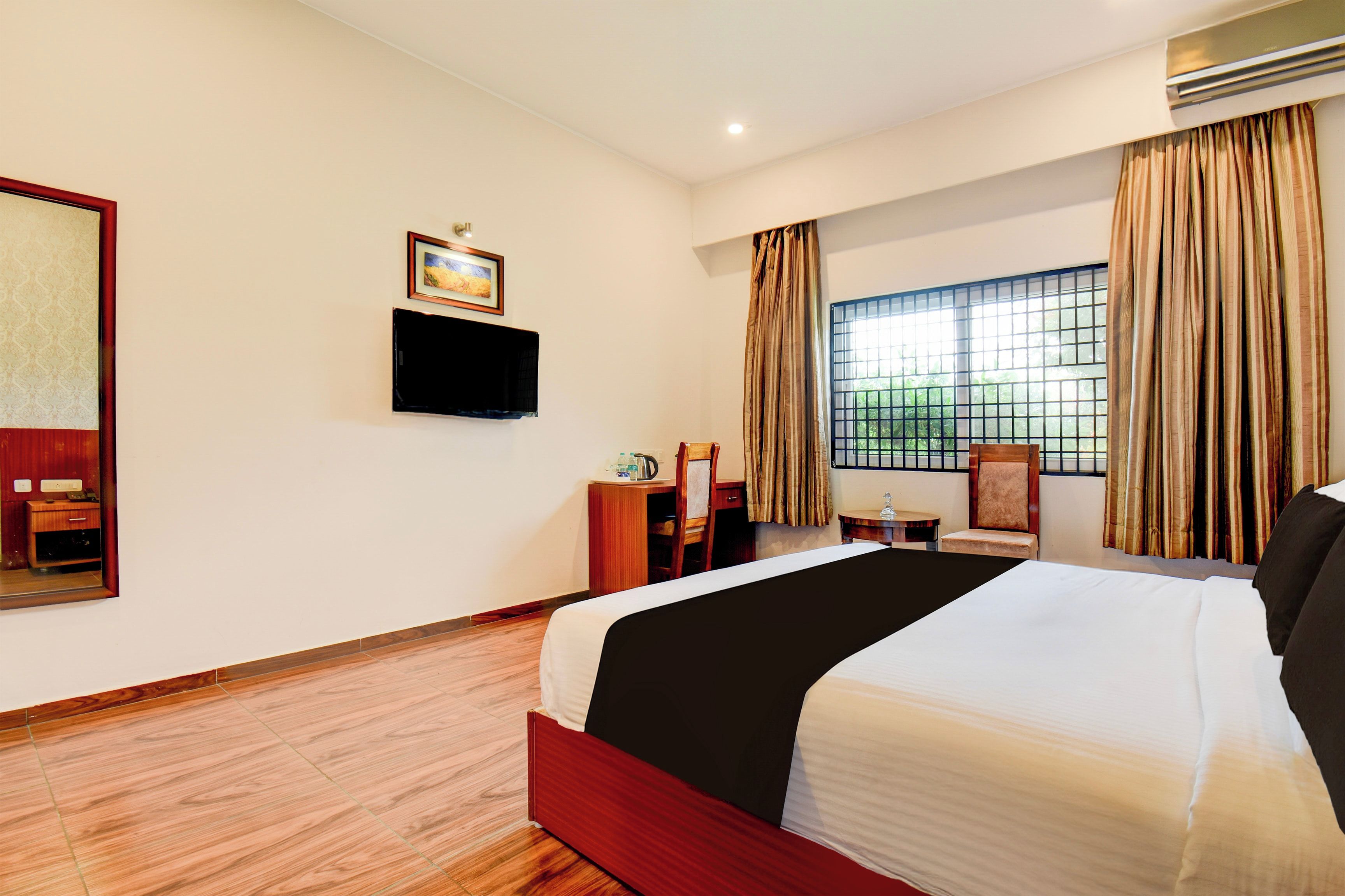 A hotel room with a bed, a television, a desk, a chair, and a window with curtains.