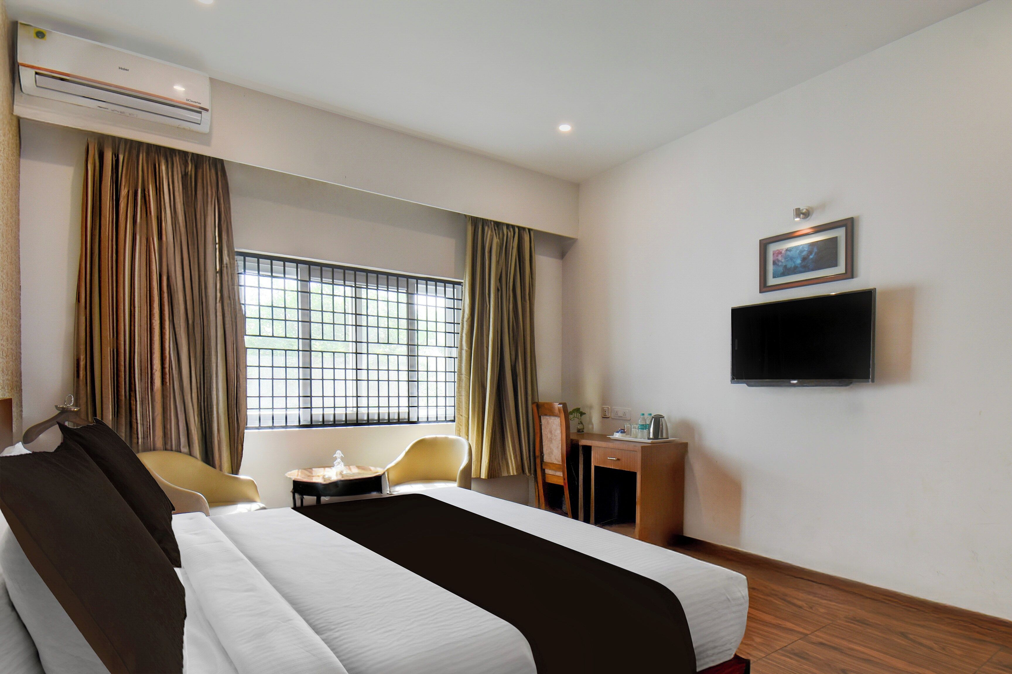 Una habitación de hotel con cama, escritorio, silla, televisor y ventana con cortinas.