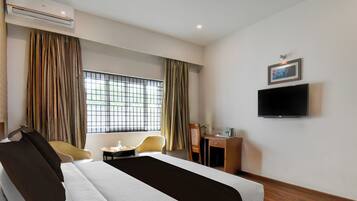 Una habitación de hotel con cama, escritorio, silla, televisor y ventana con cortinas.