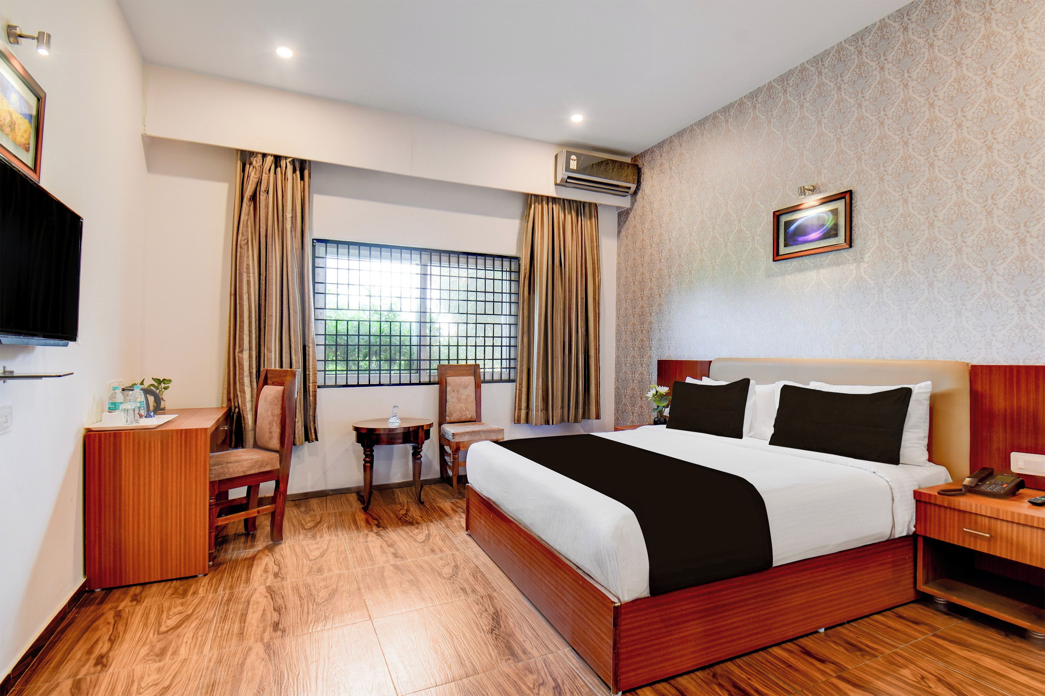 A hotel room with a bed, a desk, a chair, a small table, and a window with curtains.