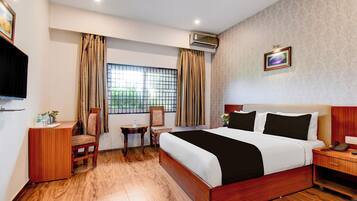 A hotel room with a bed, a desk, a chair, a small table, and a window with curtains.