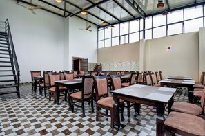 Uma ampla área de jantar com várias mesas e cadeiras, piso estampado e teto alto com luz natural.