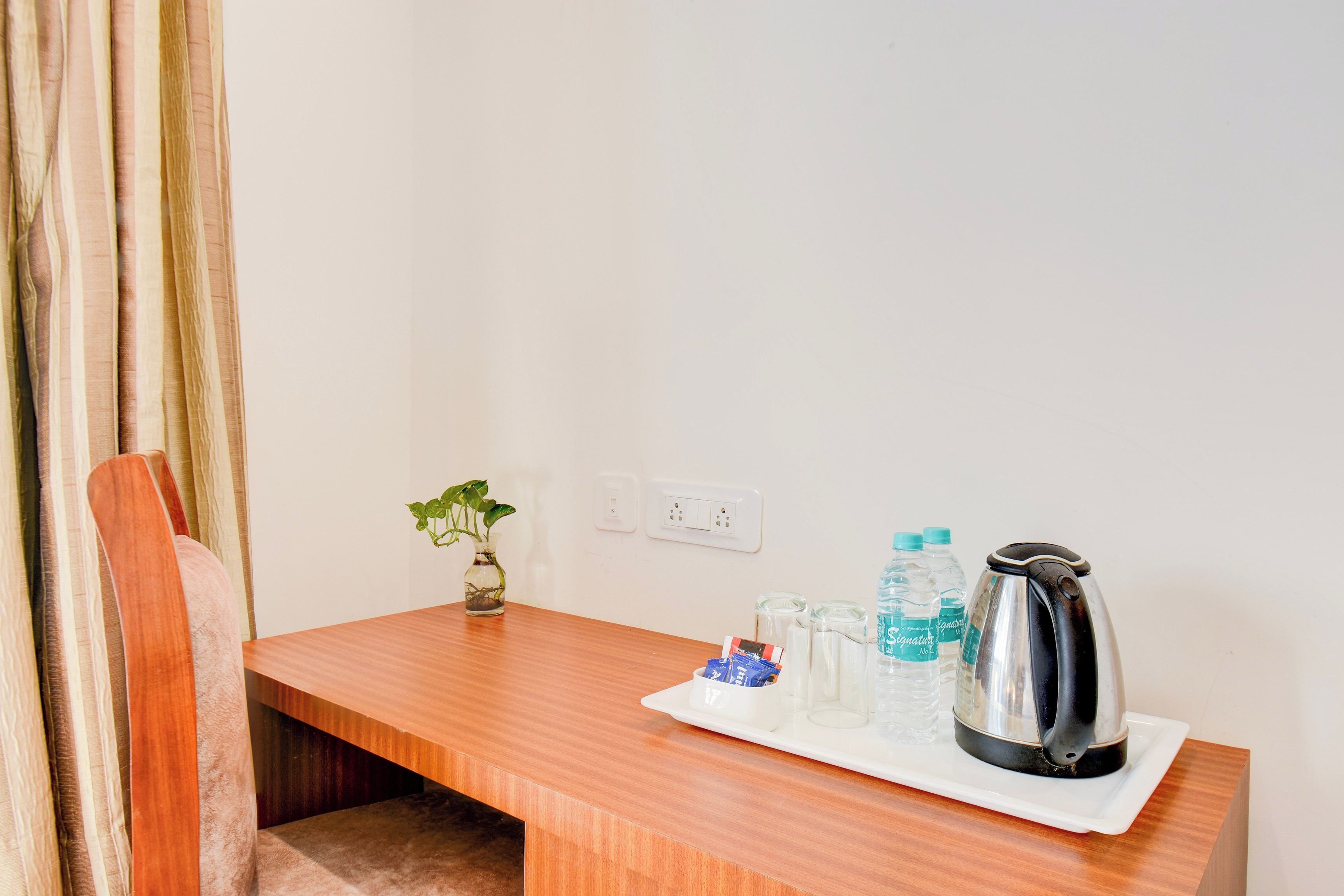 A wooden table with a small plant, a kettle, and water bottles.