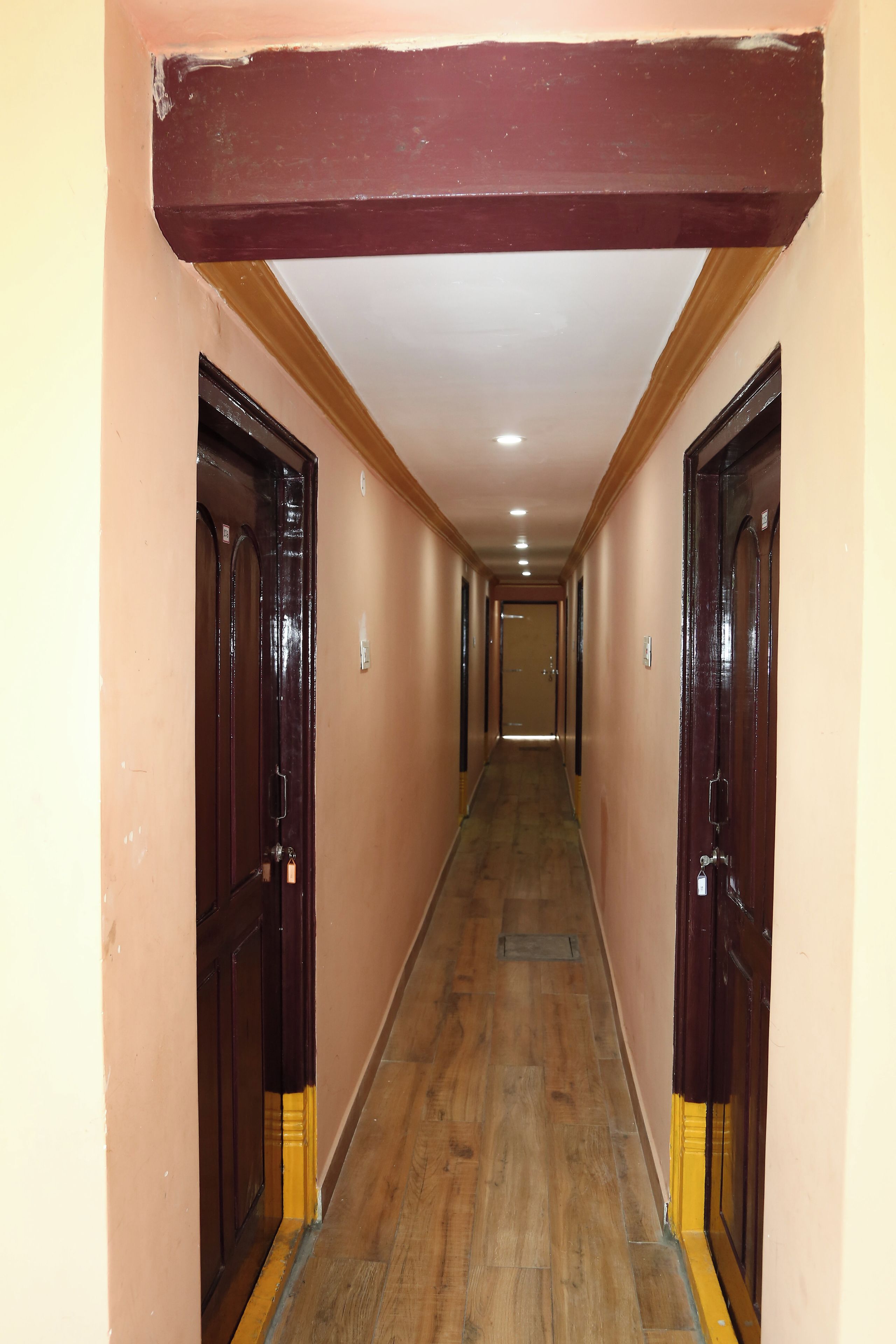 Un pasillo largo y estrecho con suelo de madera y puertas de madera oscura a ambos lados.