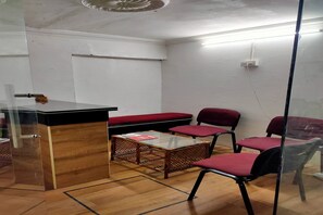 A room with a glass partition, a wooden desk, a red cushioned bench, and two red chairs.