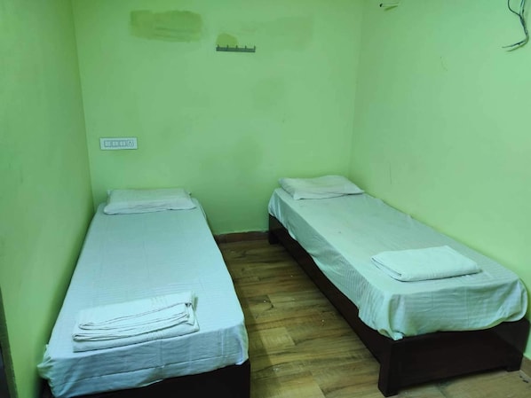 Two single beds with white linens in a small room with green walls and a wooden floor. - Spot On V GUST IN (Tenali)