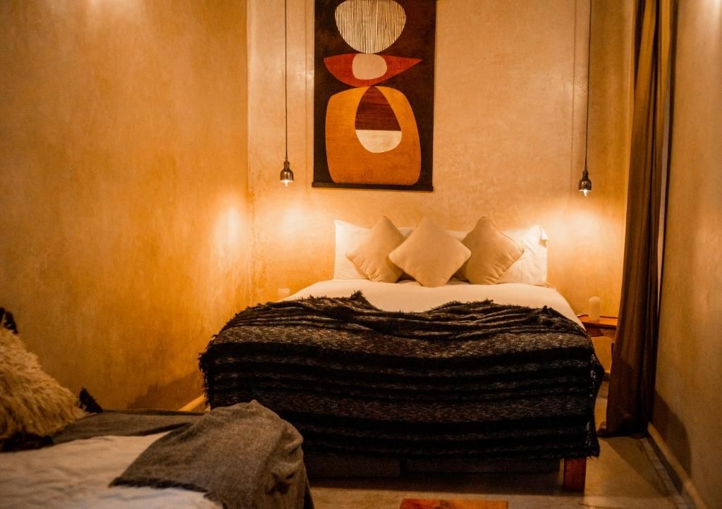 A bedroom with a bed, pillows, a blanket, a wall art piece, and two bedside lamps.