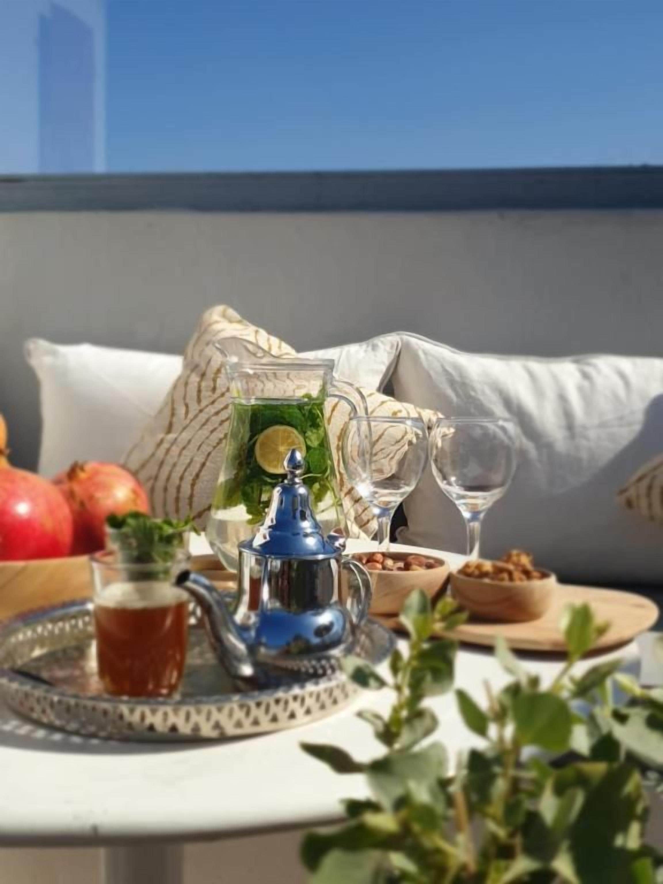 A table set with a teapot, glasses, a pitcher, and food items, suggesting a dining area with a view.