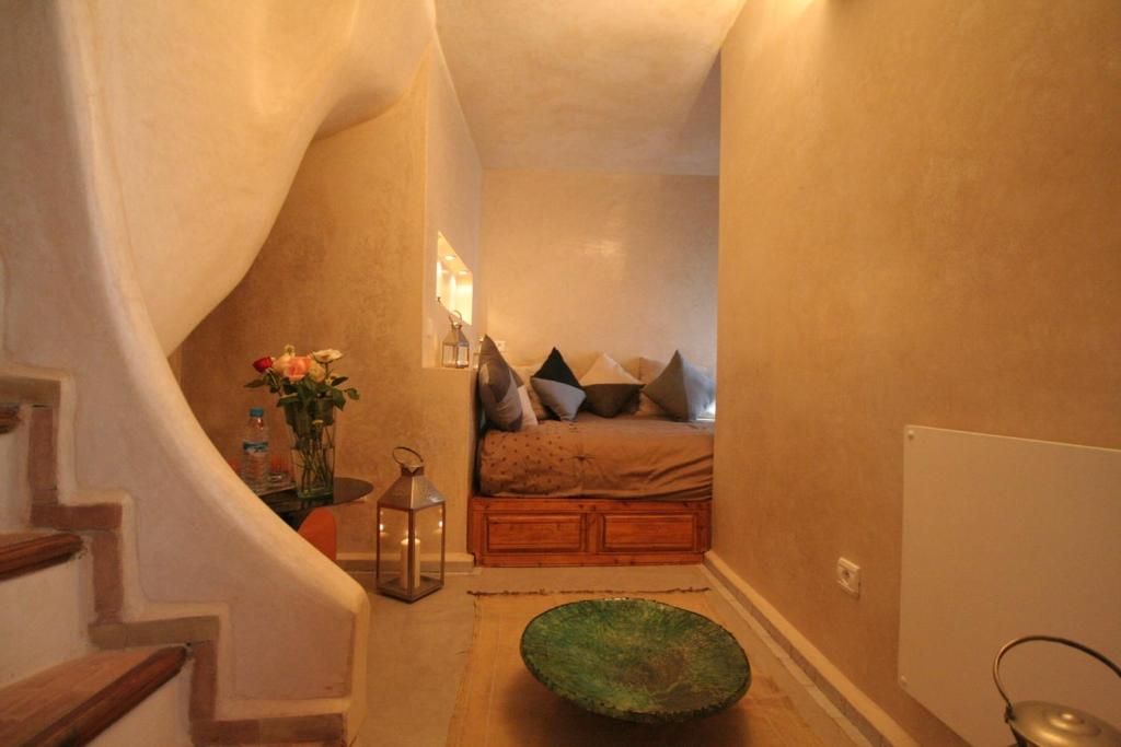 Ein schmaler Flur führt zu einem Schlafzimmer mit einem Bett, Kissen, einer Vase mit Blumen und einer Laterne.