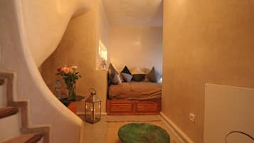 Ein schmaler Flur führt zu einem Schlafzimmer mit einem Bett, Kissen, einer Vase mit Blumen und einer Laterne.