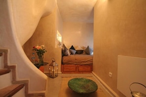 A narrow hallway leading to a bedroom with a bed, pillows, a vase with flowers, and a lantern. - Maison D'Hôtes DAR LES SIRENES (Essaouira)