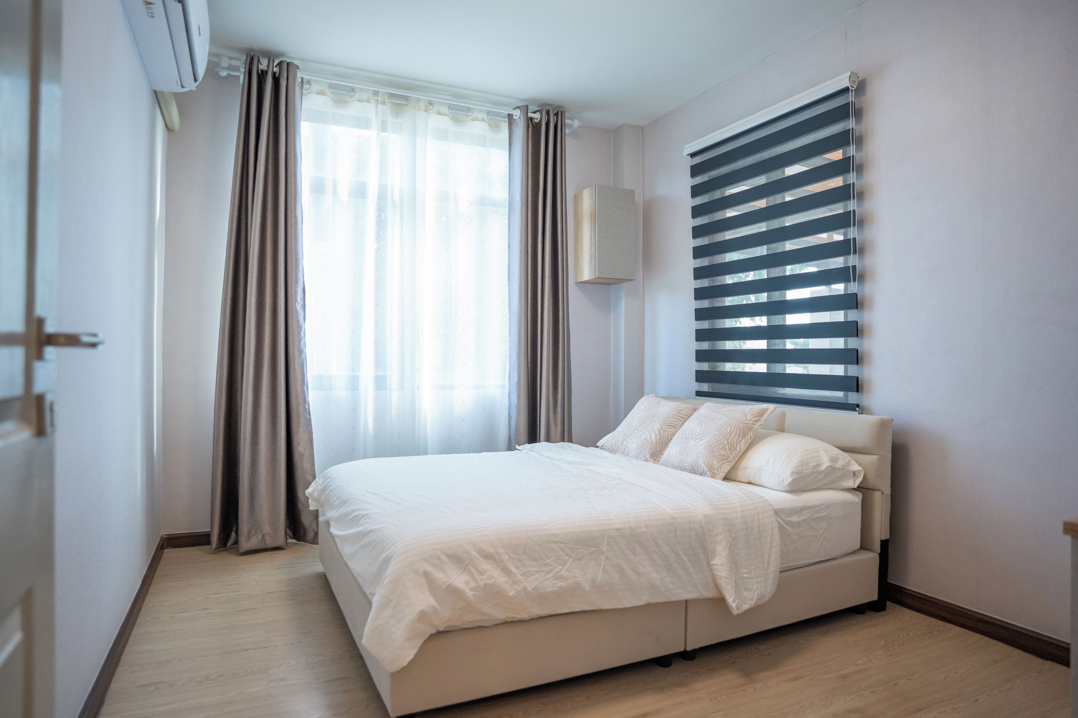 Un dormitorio con cama, cortinas, una ventana con persianas y un aire acondicionado de pared.